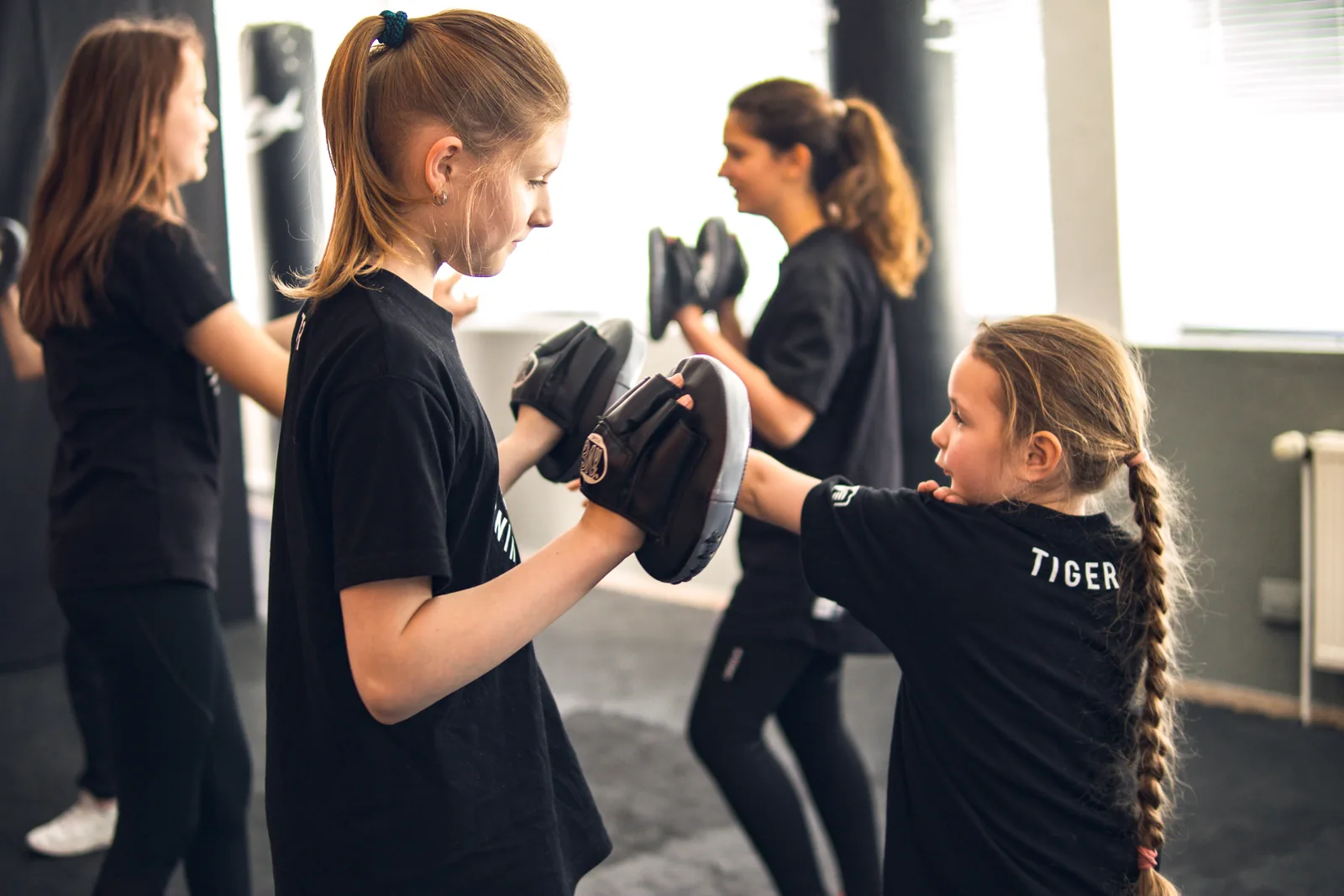 Kinder trainieren bei WTplus Bochum mit Pratzen, eines im Tiger-Shirt